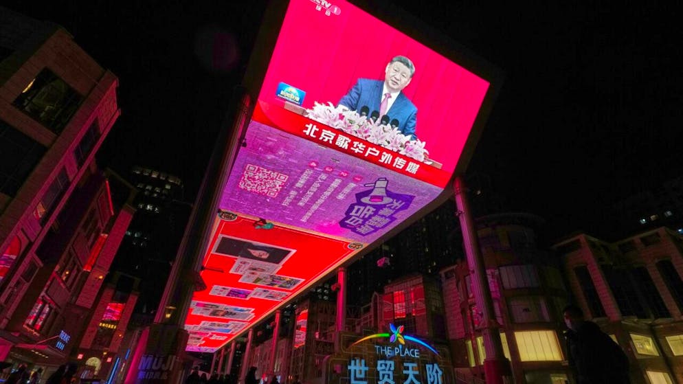 Menschen versammeln sich vor einem großen Bildschirm in einem Einkaufszentrum, auf dem CCTV die Übertragung des chinesischen Präsidenten Xi Jinping zeigt, der auch Generalsekretär des Zentralkomitees der Kommunistischen Partei Chinas und Vorsitzender der Zentralen Militärkommission ist, während er auf der Neujahrsveranstaltung des Nationalen Komitees der Politischen Konsultativkonferenz des Chinesischen Volkes (CPPCC) in Peking spricht. Foto: Andy Wong/AP/dpa