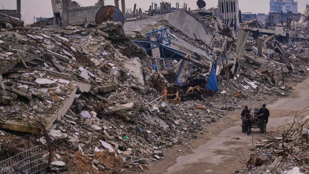 ARCHIV - Palästinenser gehen eine zerstörte Straße in der Stadt Gaza entlang (Archivbild). Foto: Abdel Kareem Hana/AP/dpa