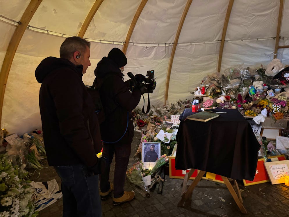 Cameraman di una troupe digiornalisti dall'estero stanno svolgendo il loro lavoro sotto la tenda dove la gente ha deposto fiori e candele in memoria delle vittime di Crans-Montana.