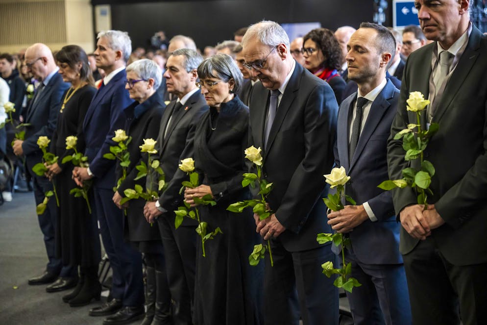La Suisse pleure. De gauche à droite : le chancelier fédéral Viktor Rossi, le conseiller fédéral suisse Beat Jans et son épouse Tracy Jans Glass, le conseiller fédéral suisse et ministre des Affaires étrangères Ignazio Cassis et son épouse Paola Cassis, le président de la Confédération suisse Guy Parmelin et son épouse Caroline Parmelin, Mathias Reynard, conseiller d'État et président du Conseil d'État du canton du Valais, Christophe Darbellay, conseiller d'État du canton du Valais, observent une minute de silence à la mémoire des victimes, lors de la cérémonie commémorative officielle et de la journée nationale de deuil qui a suivi l'incendie meurtrier du bar « Le Constellation » à Crans-Montana, au Centre d'exposition et de congrès Martigny Expo (CERM), à Martigny, en Suisse, le vendredi 9 janvier 2026. 