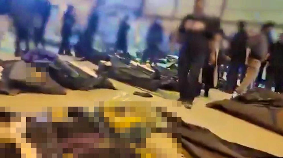 Sceenshot of a video on X: People search for relatives among rows of corpses.