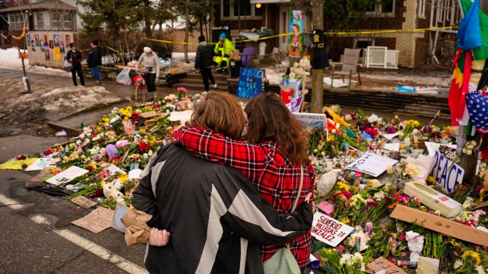 Menschen umarmen sich beim Besuch einer behelfsmäßigen Gedenkstätte für Renee Good, die letzte Woche von einem ICE-Beamten erschossen wurde. Nach den tödlichen Schüssen auf eine Frau in Minneapolis halten die Proteste gegen die US-Einwanderungsbehörde ICE an. Foto: John Locher/AP/dpa