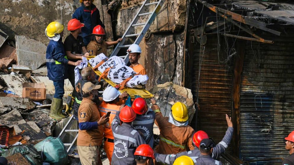 Feuerwehrleute transportieren eine Leiche, nachdem sie sie aus den Trümmern eines abgebrannten Gebäudes eines mehrstöckigen Einkaufszentrums nach einem Großbrand geborgen haben. Foto: Ali Raza/AP/dpa