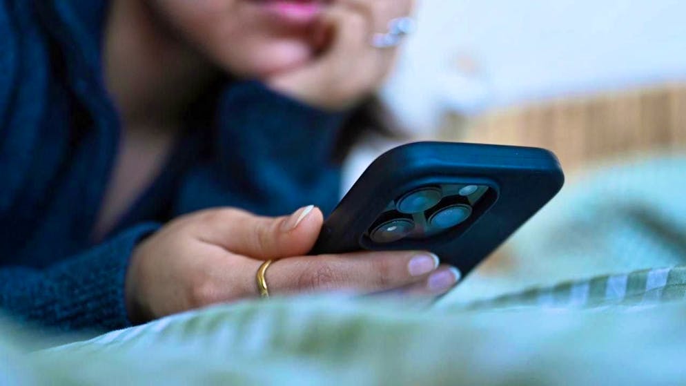 ILLUSTRATION - A young woman lies on her bed with a smartphone in her hand. Photo: Elisa Schu/dpa
