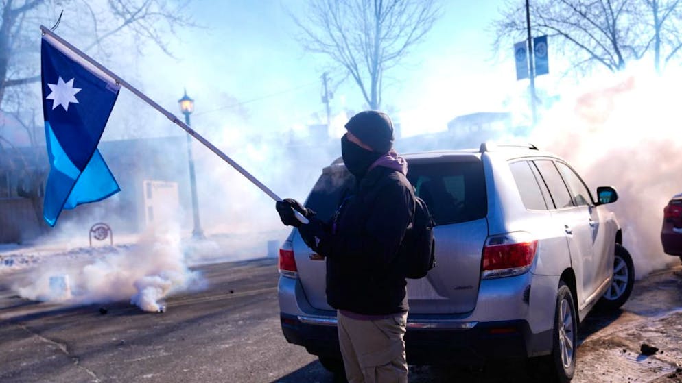 Un drapeau de l'Etat du Minnesota brandi alors que les agents fédéraux de l'immigration lancent des gaz lacrymogènes, samedi à Minneapolis.