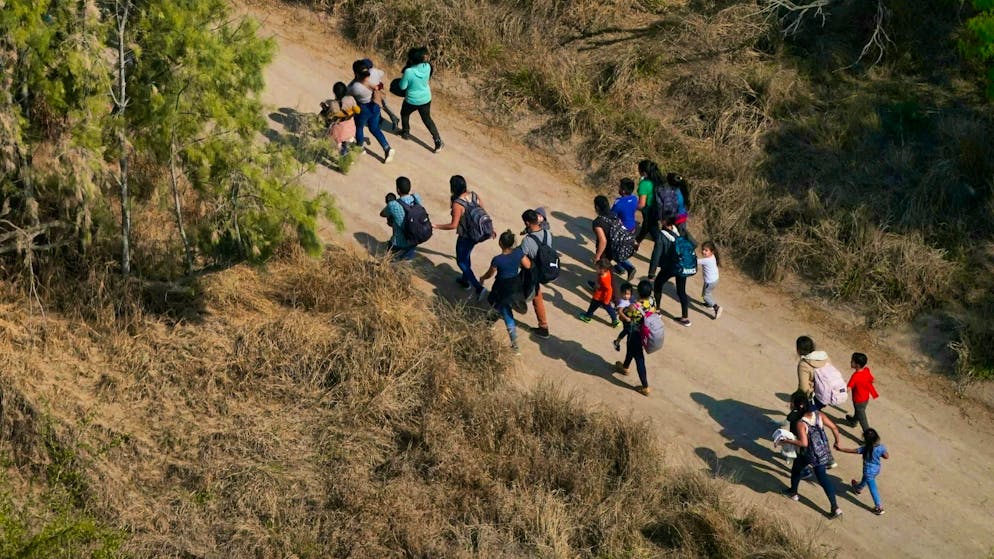 Migrants walk along a dirt road after crossing the border between the US and Mexico.