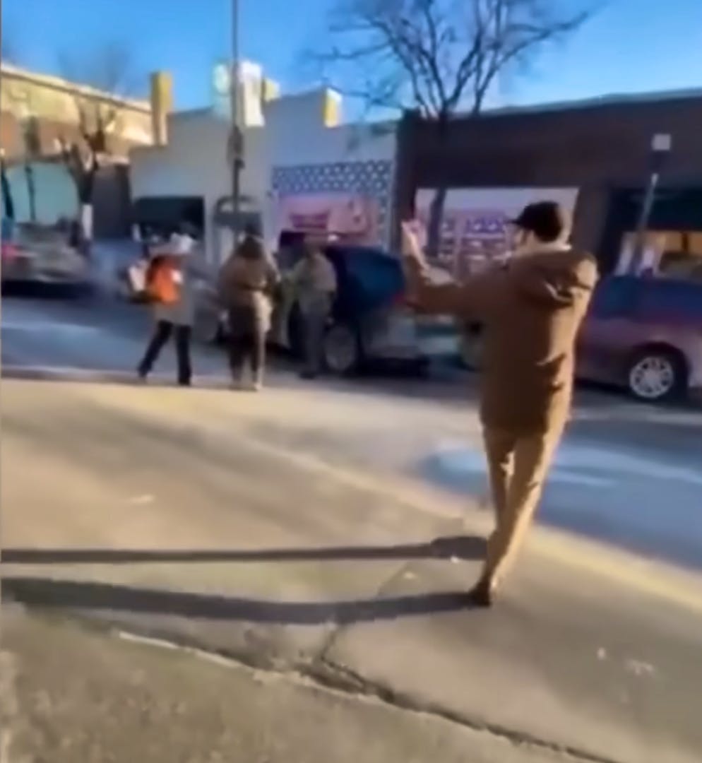 Im Hintergrund sind die ICE-Agenten zu sehen. Vorne rechts Alex Pretti, der mit dem Handy in seiner rechten Hand (verdeckt) den Vorgang filmt und mit links einem Auto, das angehalten hat, bedeutet, es könne weiterfahren.