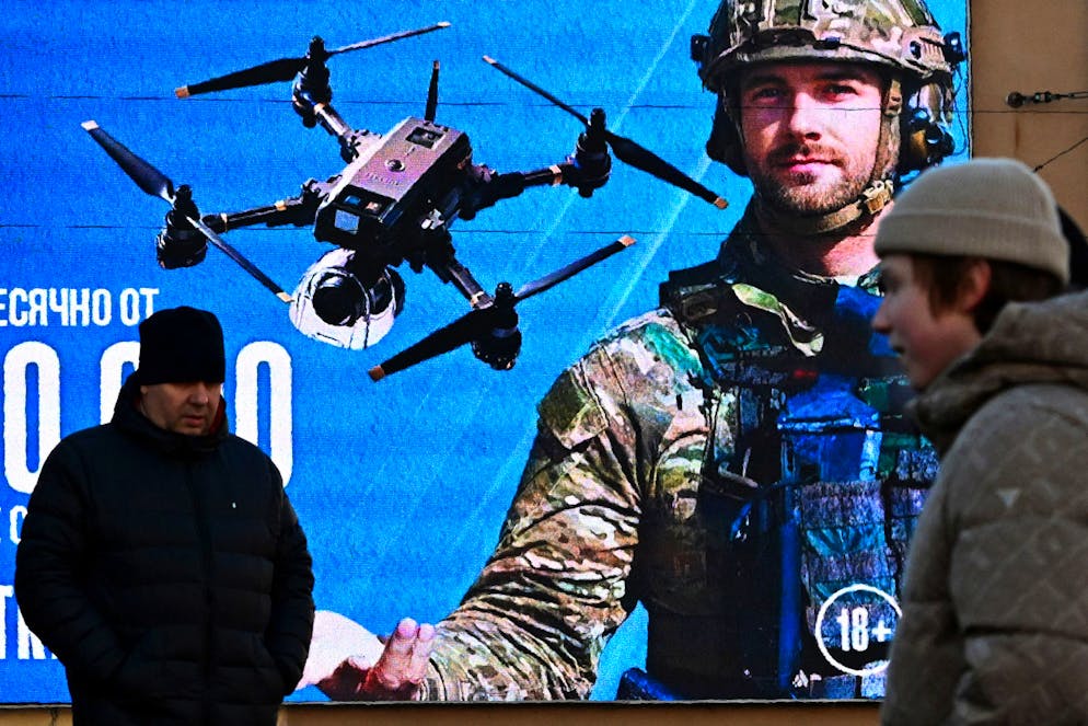 Des hommes passent devant un écran numérique affichant une publicité promouvant le service militaire contractuel dans les unités de systèmes sans pilote de l'armée russe à Saint-Pétersbourg, le 3 février 2026. (Photo par Olga MALTSEVA / AFP)