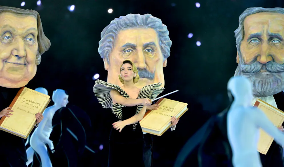 Olimpiadi 2026. La performance dell'attrice Matilde De Angelis. Dietro di lei, delle riproduzioni dei volti di Giuseppe Verdi, Giacomo Puccini e Gioacchino Rossini.