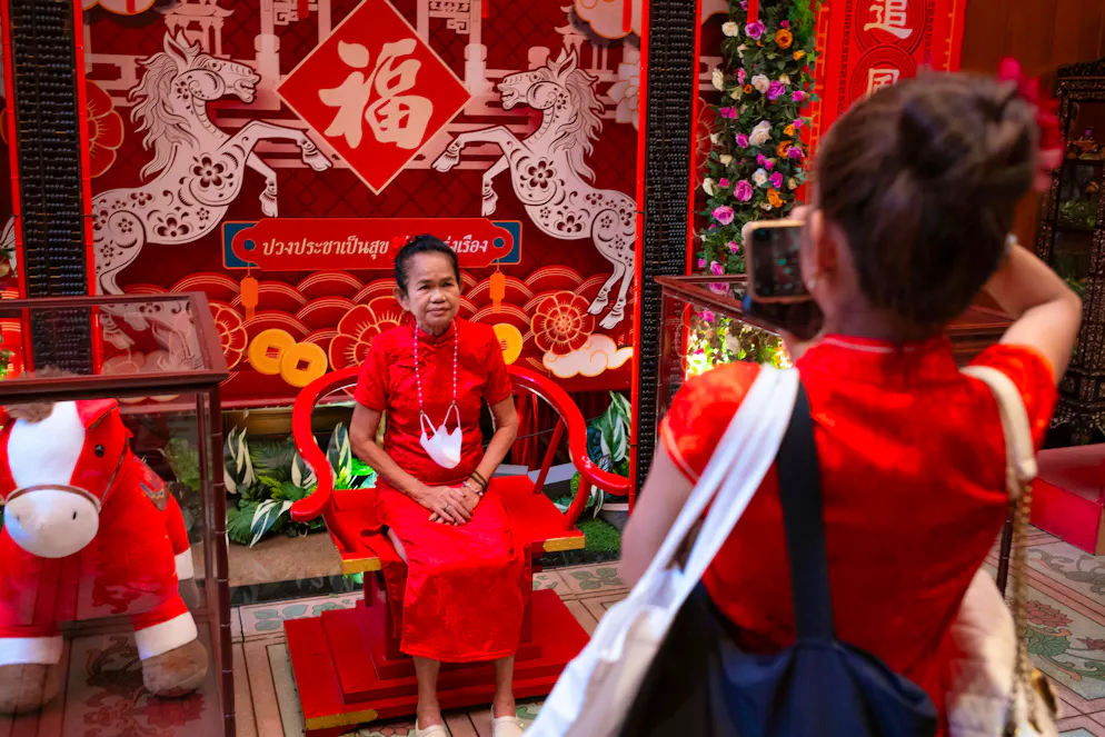 2026: Capodanno cinese sotto il segno del cavallo. Un'anziana posa davanti a un box fotografico con cavalli al Wat Mangkon Kamalawat, vicino a Yaowarat Road. Rappresentano l'anno del cavallo nello zodiaco cinese.
