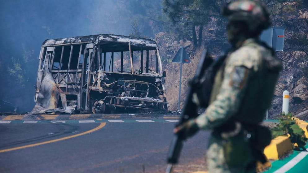 Medien: Drogenboss «El Mencho» tot – Autos brennen - Gallery. Ein Soldat steht neben einem ausgebrannten Bus, der in Cointzio nach dem Tod von «El Mencho» in Brand gesetzt wurde. 