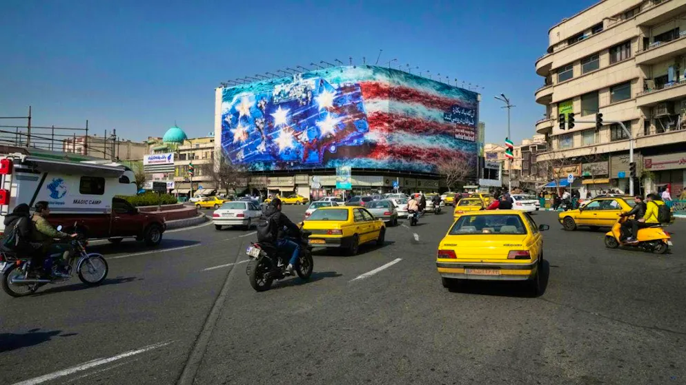Vehicles drive past a billboard depicting a US aircraft carrier with damaged fighter jets on deck. On Enqelab-e-Eslami Square (Square of the Islamic Revolution), the words "He who sows wind will reap storm" are written in Farsi and English. Photo: Vahid Salemi/AP/dpa