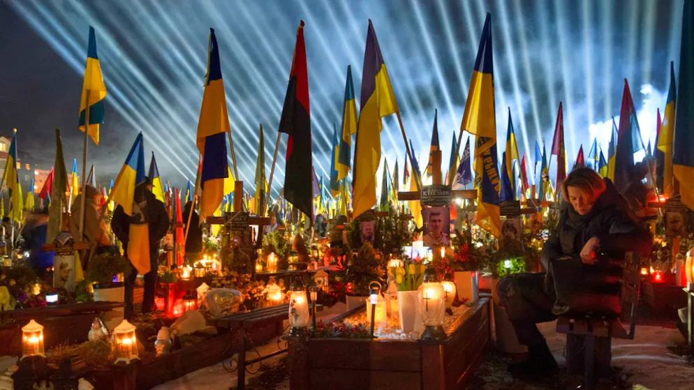 Flutlichter leuchten über den Gräbern der gefallenen Soldaten, während Menschen am Vorabend des vierten Jahrestages der russischen Invasion Kerzen anzünden. Foto: Mykola Tys/AP/dpa