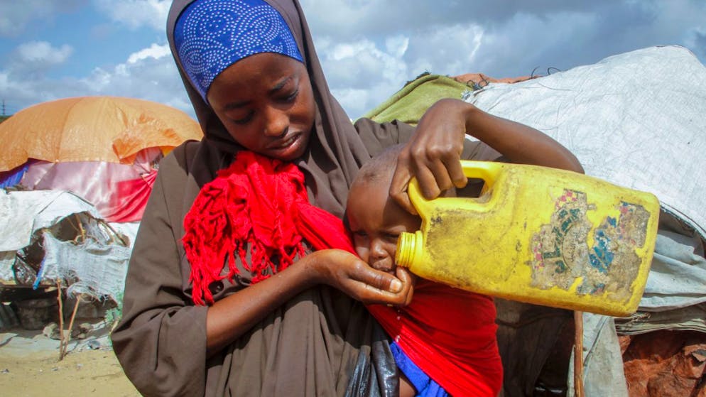 ARCHIV - Eine somalische Frau, die aus den von der Dürre betroffenen Gebieten geflohen ist, gibt ihrem Kind Wasser aus einem Plastikbehälter in einem Lager für Vertriebene am Stadtrand von Mogadischu. Foto: Farah Abdi Warsameh/AP/dpa