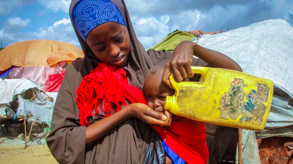 ARCHIVE - A Somali woman who fled drought-affected areas gives her child water from a plastic container at a camp for displaced people on the outskirts of Mogadishu. Photo: Farah Abdi Warsameh/AP/dpa