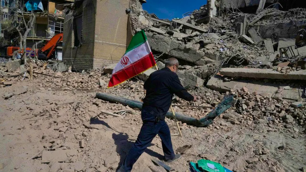 A man carries an Iranian flag and places it on the rubble of a police facility that was hit during the US-Israeli military action. Photo: Vahid Salemi/AP/dpa