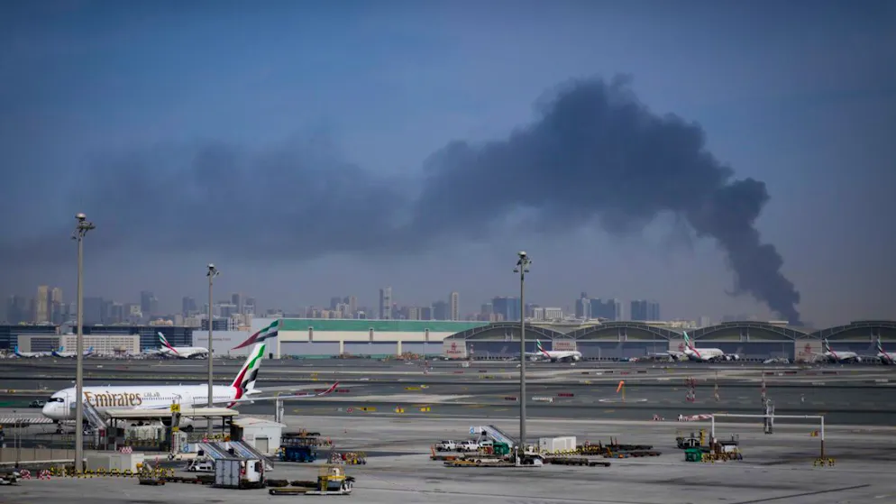ARCHIV - Eine Rauchwolke, verursacht durch einen iranischen Angriff, ist im Hintergrund zu sehen, während Flugzeuge der Emirates nach der Schließung des Flughafens auf dem Dubai International Airport geparkt sind. Foto: Altaf Qadri/AP/dpa