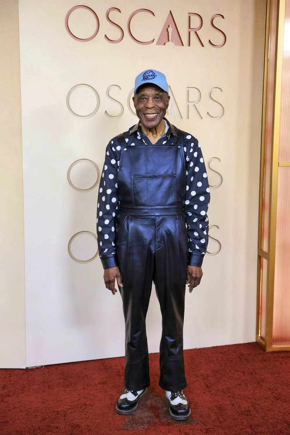 Oscar 2026: i migliori abiti del red carpet. Buddy Guy mescola pois retrò e salopette in pelle. Tappeto rosso? Non importa: il cappello rimane.