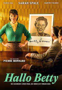 Eine Frau in einem grünen Cardigan steht selbstbewusst in einem Büro vor einem Plakat der fiktiven Figur 