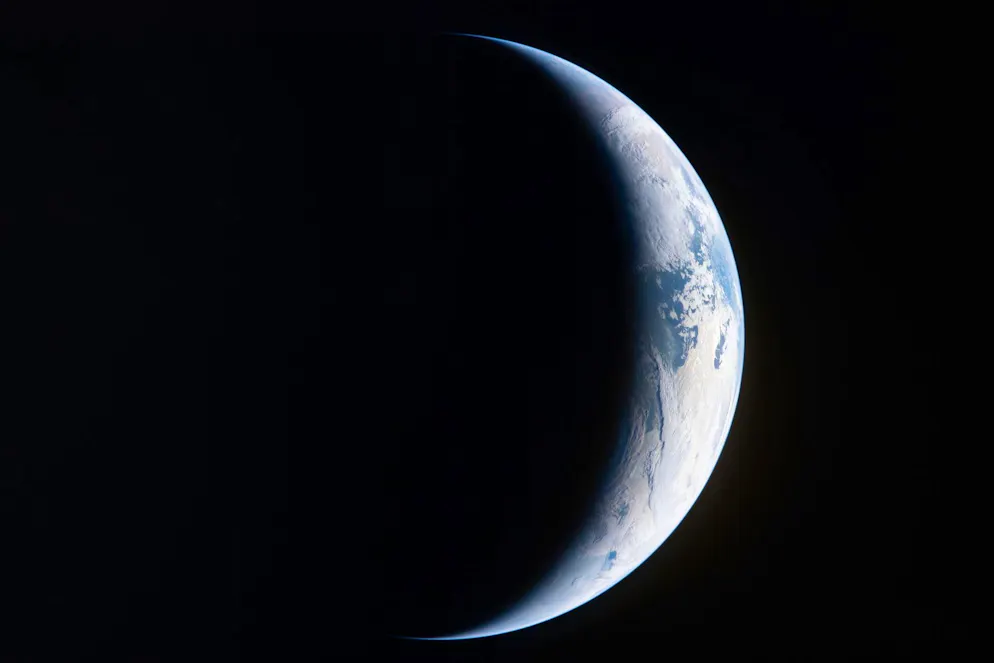 Durch ein Fenster der Orion‑Raumkapsel hält ein Mitglied der Artemis‑II‑Besatzung die strahlende Erde im Dunkel des Alls fest.