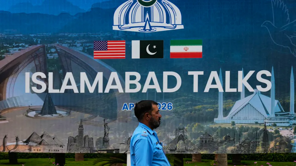 Ein Polizeibeamter geht vor einem Medienzentrum an einer Plakatwand zu den Verhandlungen zwischen den USA und dem Iran vorbei. Foto: Anjum Naveed/AP/dpa