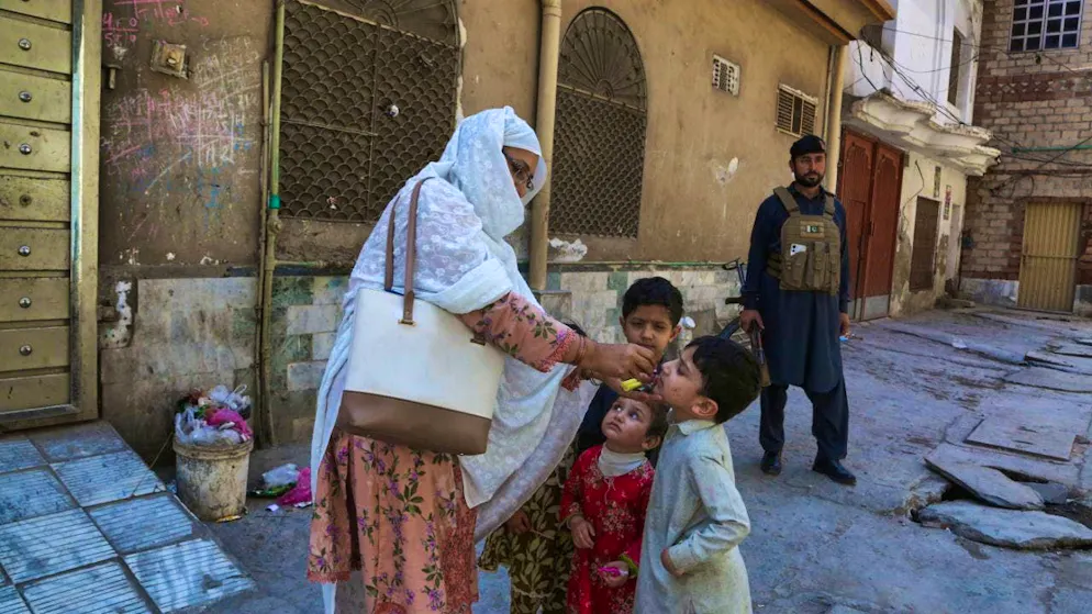 یک پلیس نگهبانی می‌دهد در حالی که یک کارمند صحی در حال تزریق واکسن فلج اطفال به کودکی در منطقه‌ای مسکونی در پیشاور، پاکستان است. عکس: محمد سجاد/AP/dpa