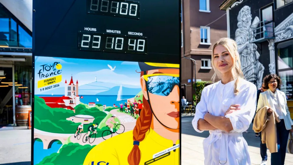 Marion Rousse, die Direktorin der Tour de France Femmes, steht neben der Affiche für die Austragung 2026 mit dem Countdown in Lausanne