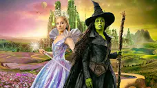 Ariana Grande als Glinda in einem rosa Kleid und Cynthia Erivo als grün-häutige Elphaba in Hexenkleidung vor der Smaragdstadt in der Verfilmung von Wicked.
