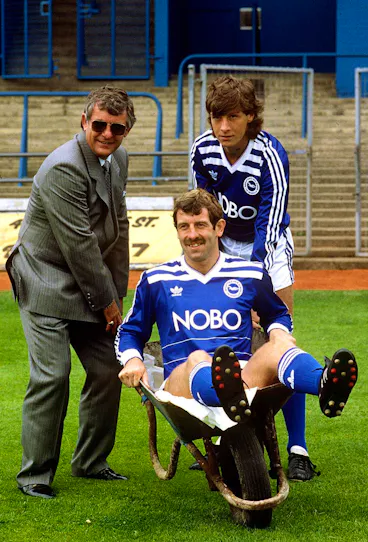 Bildnummer: 03391352  Datum: 01.08.1986  Copyright: imago/Colorsport
Trainer Alan Mullery (li.) und Dale Jasper (re.) mit Gerry Armstrong (alle Brighton) in der Schubkarre - PUBLICATIONxINxGERxSUIxAUTxHUNxUSAxONLY; Brighton and Hove Albion, Vdia, hoch, Präsentation, Pressetermin, Fotoshooting, Karre, sitzen English Football League Second Division 1986/1987, Two, 2. Englische Liga Brighton Komik,  Fußball Herren Mannschaft England Gruppenbild optimistisch Randmotiv Personen Objekte Kurios