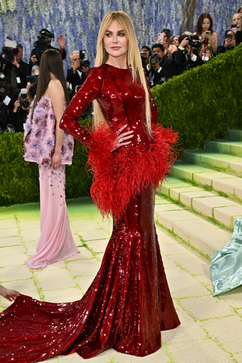 MET Gala – die Looks vom roten Teppich. Ein Griff in die Faschingskiste? Nicole Kidman hat jedenfalls keine Scheu davor, auffällige Elemente wie Pailletten und Federn zu mixen – alles in einem Rot-in-Rot-Spiel. Trotzdem gelingt es ihr, den Look elegant wirken zu lassen, nicht zuletzt, weil sie kaum Haut zeigt und die Silhouette geschlossen hält. Dazu trägt sie ihr Haar minimalistisch geglättet.