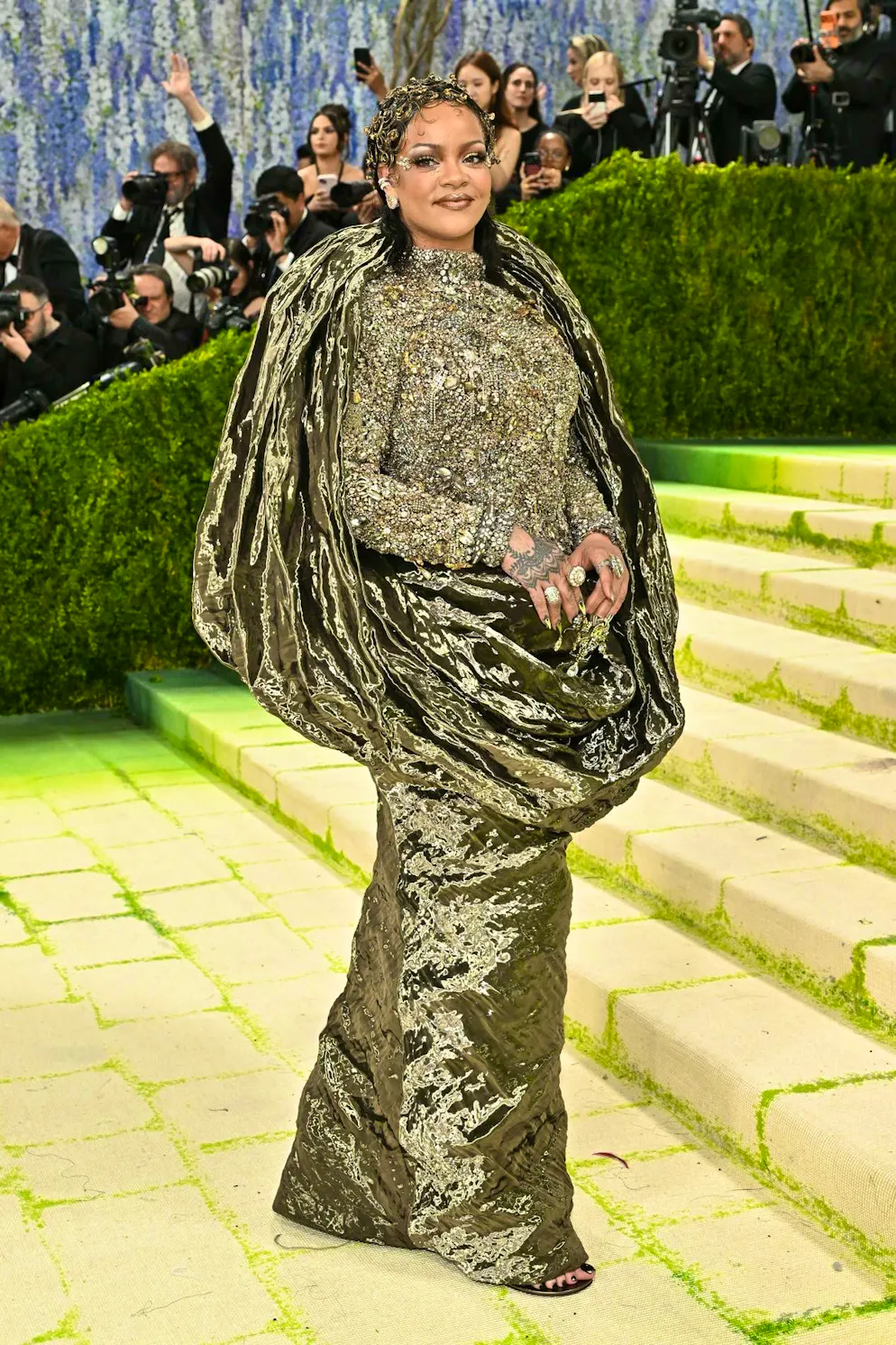 MET Gala - les looks du tapis rouge. Rihanna opte pour un look métallique – et, une fois encore, pour un volume maximal grâce à des drapés opulents. Mais face aux centaines de milliers de perles de cristal, de bijoux anciens et de chaînes qui recouvrent son haut, le terme « métallique » paraît presque… sous-estimé.