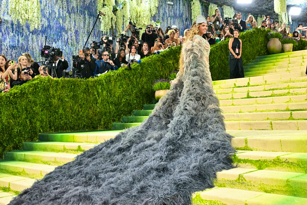 MET Gala - les looks du tapis rouge. En contraste avec l’éclat froid, elle porte un manteau d’opéra chiné gris-beige à la traîne surdimensionnée – quelque part entre gothique chic et élégance royale.