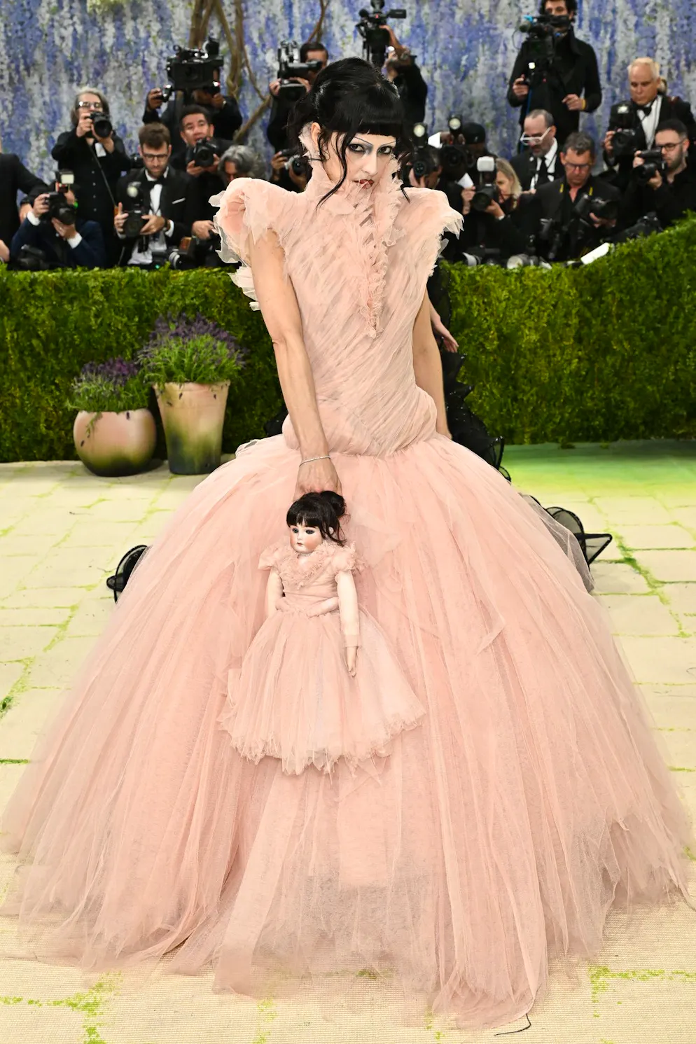 MET Gala – die Looks vom roten Teppich. María Zardoya setzt auf einen auffälligen Kontrast: Ein altrosafarbenes Tüllkleid trifft auf dunkles Make-up und tiefschwarze Haare – im Partnerlook mit ihrer Puppe. Ein Auftritt zwischen verspielter Romantik und leicht düsterer Inszenierung, der bewusst mit Gegensätzen arbeitet.
