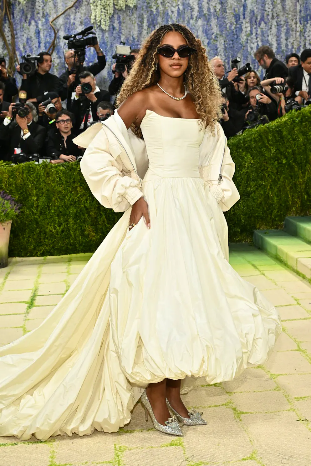 MET Gala – die Looks vom roten Teppich. Blue Ivy Carter hatte kiene Lust auf Exzentrik und zeigt lieber einen tragbaren Look: Sie trägt den angesagten Ballon-Jupe in Midi-Version, kombiniert mit passendem Mantel – alles in zartem Pastellgelb. Dazu glitzernde Schuhe, natürliche Wellen und eine Sonnenbrille. Ein Auftritt, der eher nach stilbewusstem Alltag als nach Kostüm aussieht.