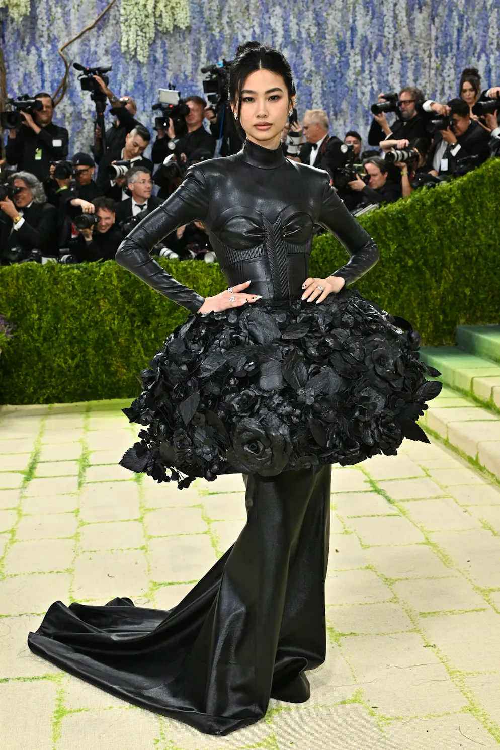 MET Gala – die Looks vom roten Teppich. Das Südkoreanische Model Jung Ho-yeon liefert einen beeindruckenden Auftritt in einem Ganzkörper-Leder-Dress mit integriertem Korsett und übertriebenem Peplum mit dreidimensionalen Blumen für maximale Hüftbetonung – ein Look, der klar auf Struktur, Härte und dramatische Silhouette setzt.