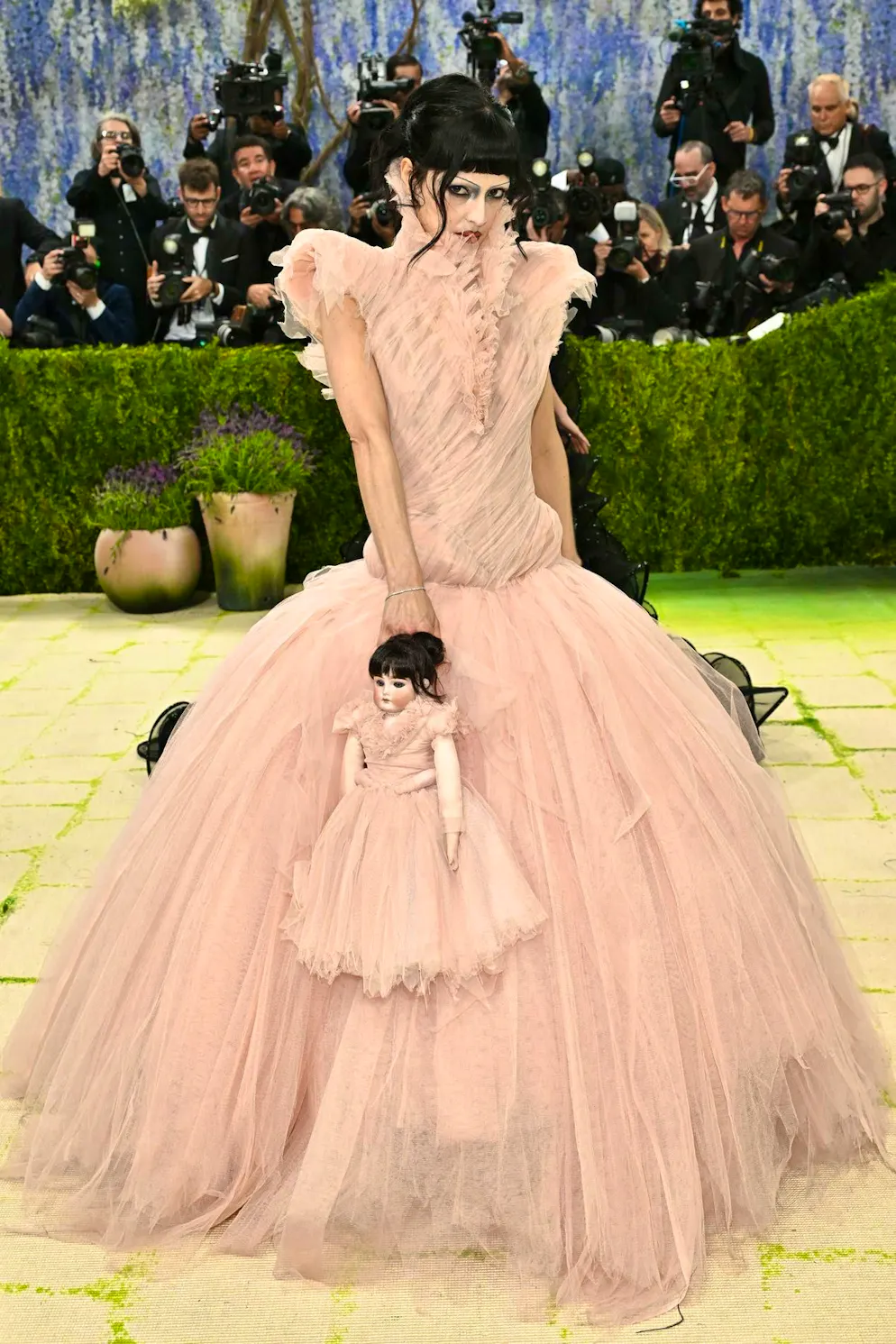 MET Gala - les looks du tapis rouge. María Zardoya joue sur un contraste saisissant : une robe en tulle vieux rose associée à un maquillage sombre et des cheveux d’un noir profond, le tout en duo assorti avec sa...  poupée! Une apparition entre romantisme délicat et mise en scène légèrement ténébreuse, qui exploite volontairement les oppositions.