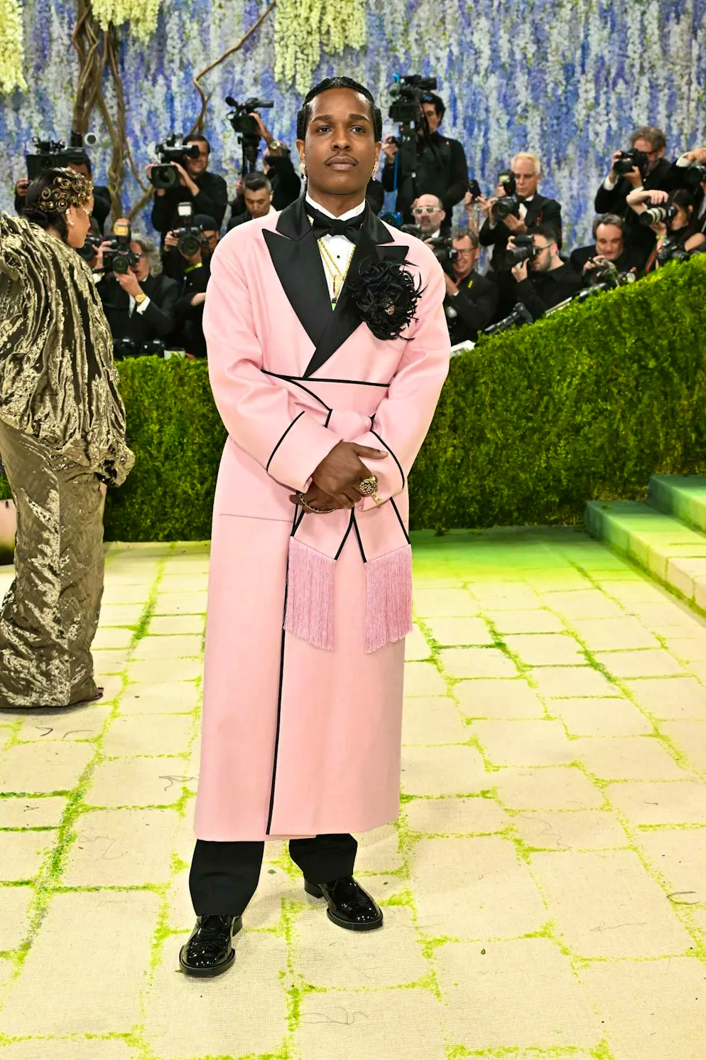 MET Gala - les looks du tapis rouge. A$AP Rocky mise sur le rose et souligne sa taille avec un look Chanel sur mesure. Plumes, satin et passepoils servent d’éléments décoratifs et confèrent à l’ensemble une opulence raffinée. Un jeu subtil entre codes féminins et masculins, volontairement discret mais parfaitement maîtrisé.