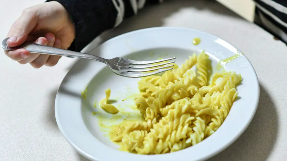 ARCHIV – Ein Kind isst Nudeln von einem Teller. Was Menschen essen, hat auch damit zu tun, was sie sich leisten können. Foto: Jens Kalaene/dpa-Zentralbild/dpa