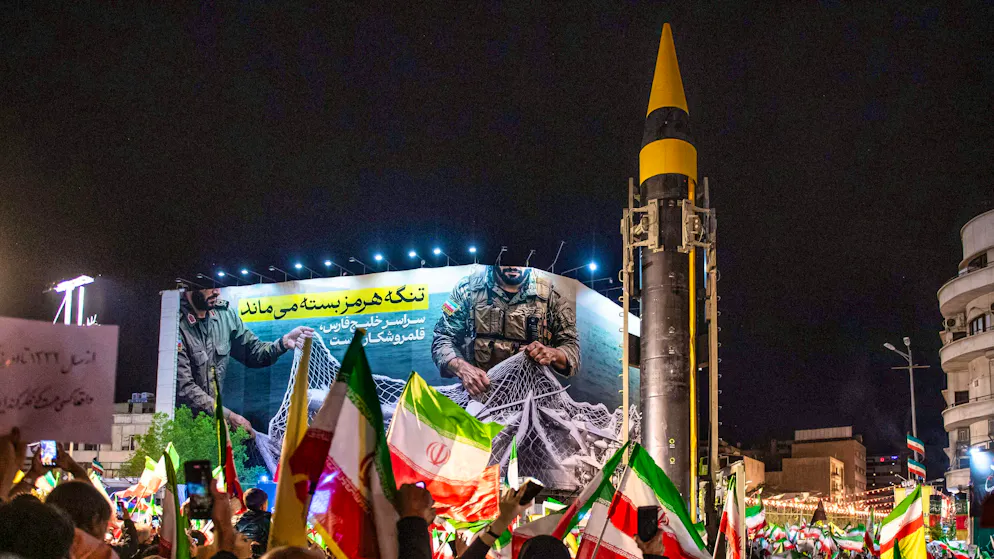 A ballistic missile is displayed by the Iranian Revolutionary Guard during a pro-government demonstration in Tehran on April 21, 2026 - behind it a propaganda poster about the battle for the Strait of Hormuz.