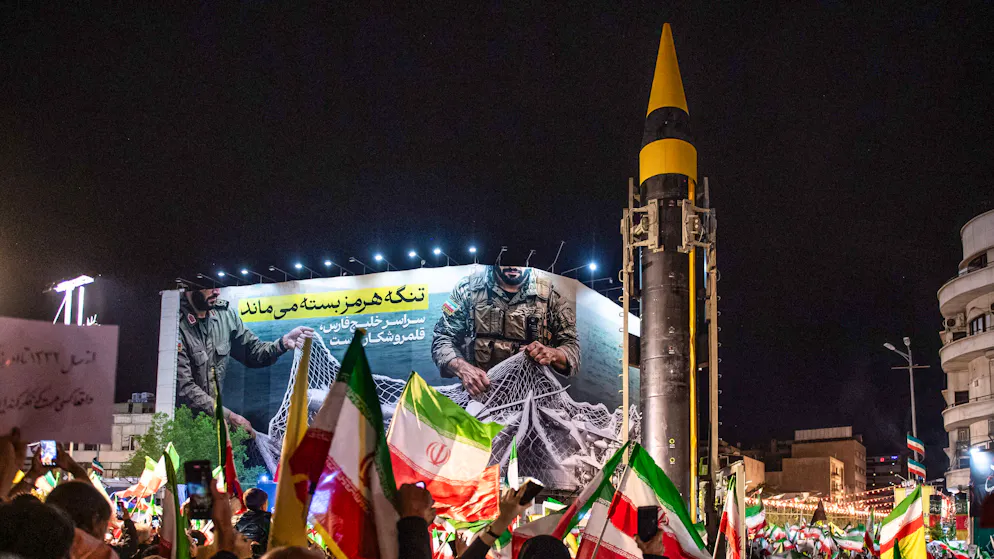 Eine ballistische Rakete wird  am 21. April 2026 von der iranischen Revolutionsgarde während einer regierungsfreundlichen Demonstration in Teheran ausgestellt – dahinter ein Propagandaplakat zum Kampf um die Strasse von Hormus.