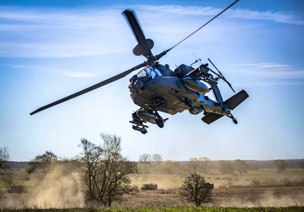 A Boeing AH-64 Apache combat helicopter of the Dutch armed forces flies in front of Bandvagn 206 all-terrain vehicles during the Aurora 26 maneuver near Lund in Sweden on April 29.