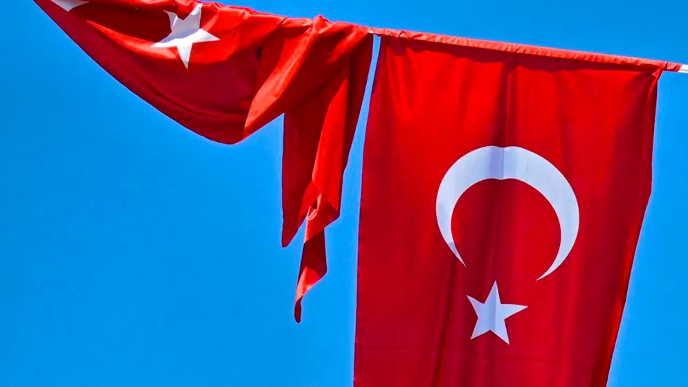 ARCHIVE - A Turkish flag flies in the wind against a blue sky, while a second flag hangs wound up next to it. Photo: Anna Ross/dpa/symbol