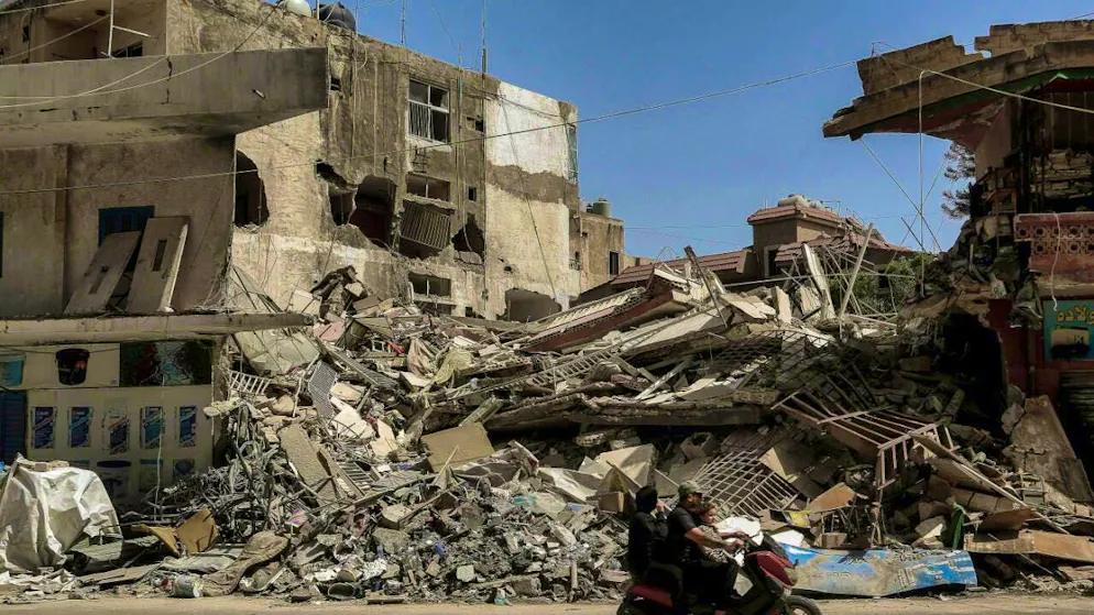 A Lebanese family rides a motorcycle past destroyed buildings hit by Israeli airstrikes in the southern port city of Tyre. Photo: Marwan Naamani/dpa