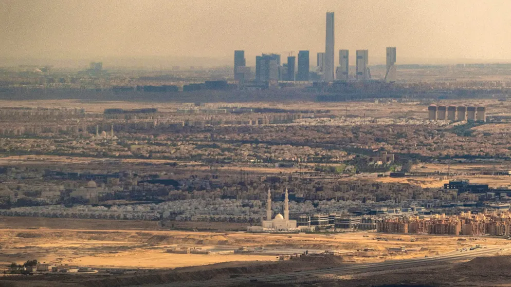Aerial view from February 16, 2024: In the foreground, extensive residential compounds in the desert, behind them the skyline of the new Egyptian capital with the "Iconic Tower" and modern skyscrapers.