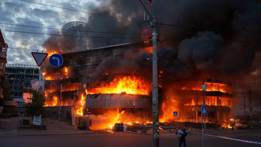 dpatopbilder – Ein Mann trägt eine Kiste aus einem brennenden Handelszentrum nach einem russischen Angriff auf Kiew. Foto: Evgeniy Maloletka/AP/dpa