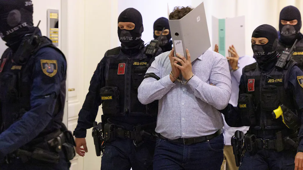 Zwei Angeklagte verbergen ihre Gesichter hinter Aktenordnern auf dem Weg in den Gerichtssaal des Landesgericht in Wien am 28. Mai 2026.