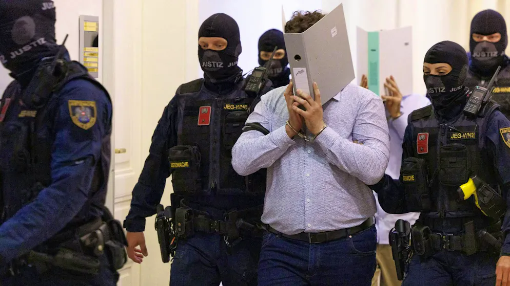 Two defendants hide their faces behind folders on their way into the courtroom of the regional court in Vienna on May 28, 2026.