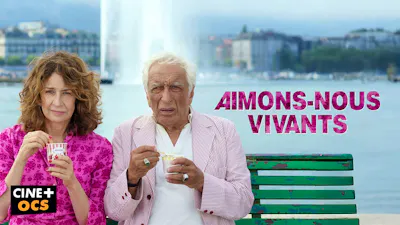 Frau und älterer Mann essen Eis auf einer Parkbank vor einer Wasserfontäne.