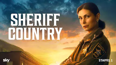 Beamtin in Sheriff-Uniform blickt entschlossen in die Kamera vor abendlichem Himmel.