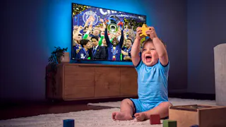 Kleinkind hält begeistert einen gelben Stern hoch, während im Hintergrund auf dem Fernseher die Siegerehrung der UEFA Champions League läuft.